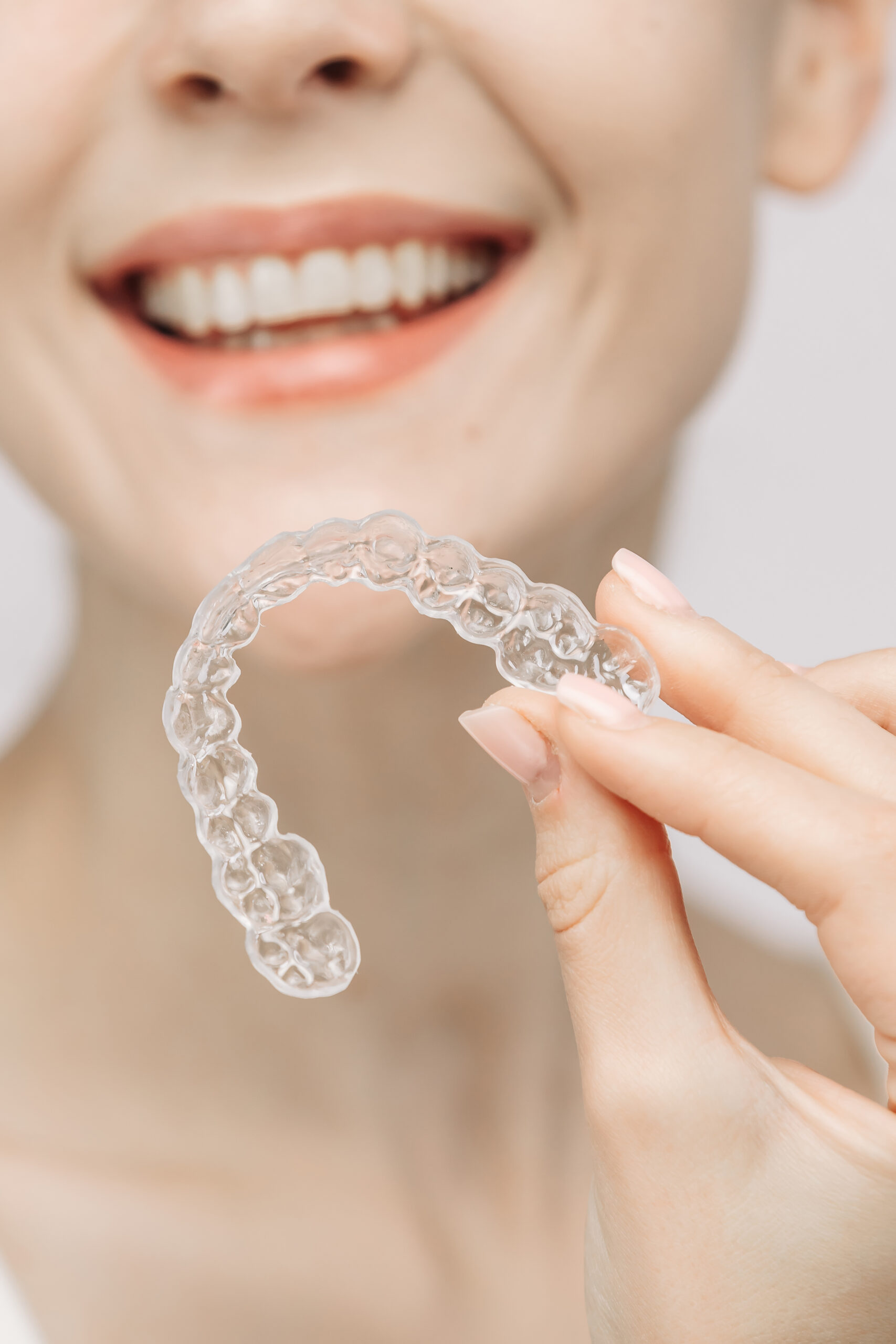 A woman with a beautiful smile and healthy teeth wears an orthodontic silicone trainer. This invisible aligner showcases a modern approach to orthodontics and confidence in her appearance.