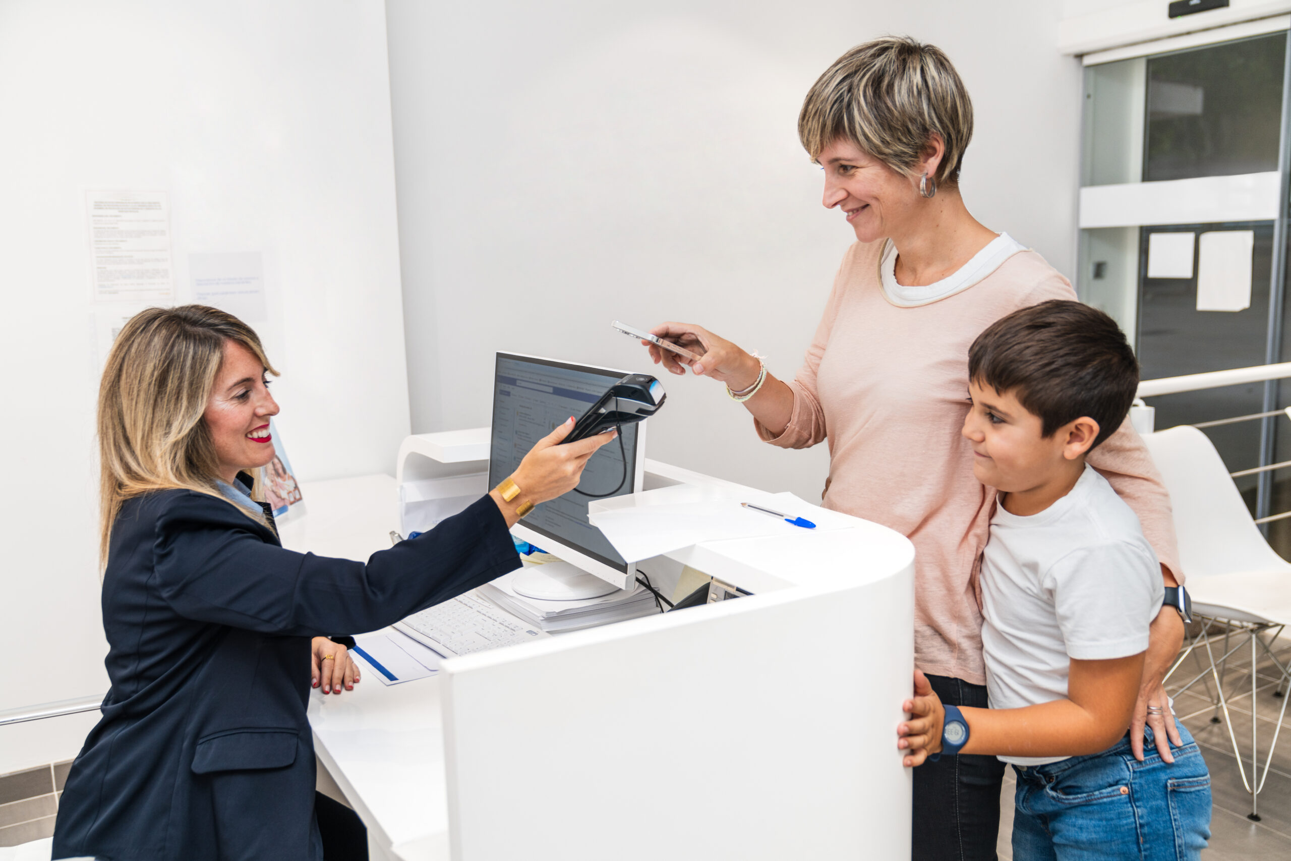 A mother and her son are seen paying at a dental clinic's reception desk, interacting with the receptionist. Concept of payment and customer service.