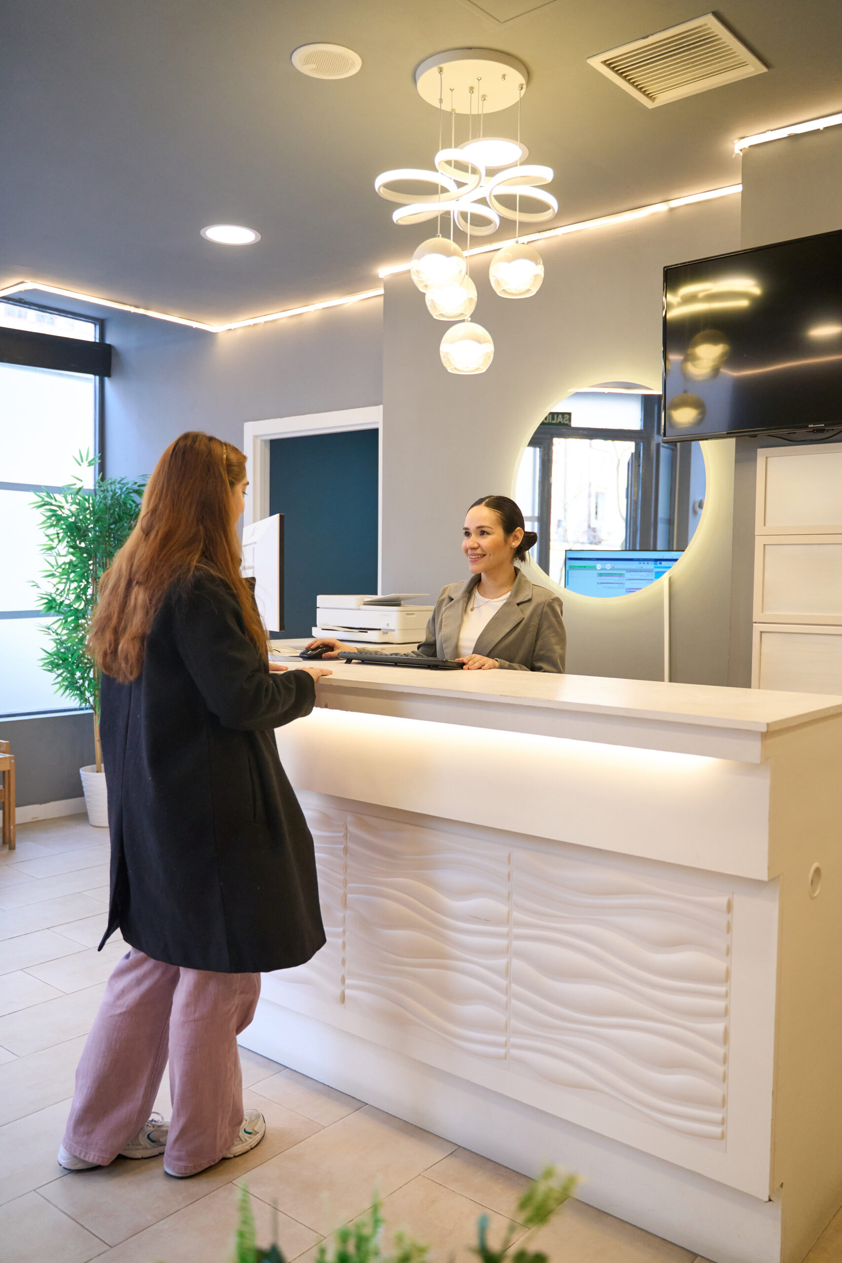 Patient communicating with receptionist at the front desk of a modern dental clinic, discussing appointment details and paperwork