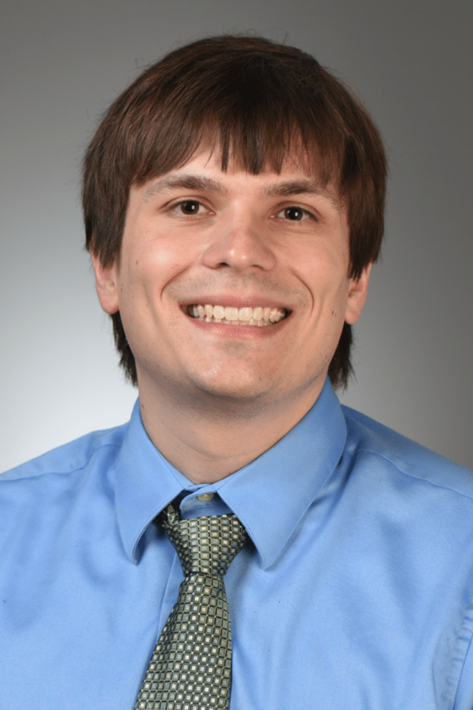 Portrait of Dr. Austin Hughes smiling with a blue shirt and green tie.